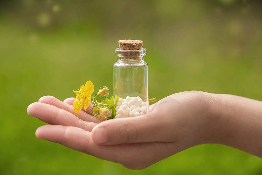 Behandlung Homoeopathie Eine Hand hält ein Gläschen mit Globuli und eine gelbe Blume